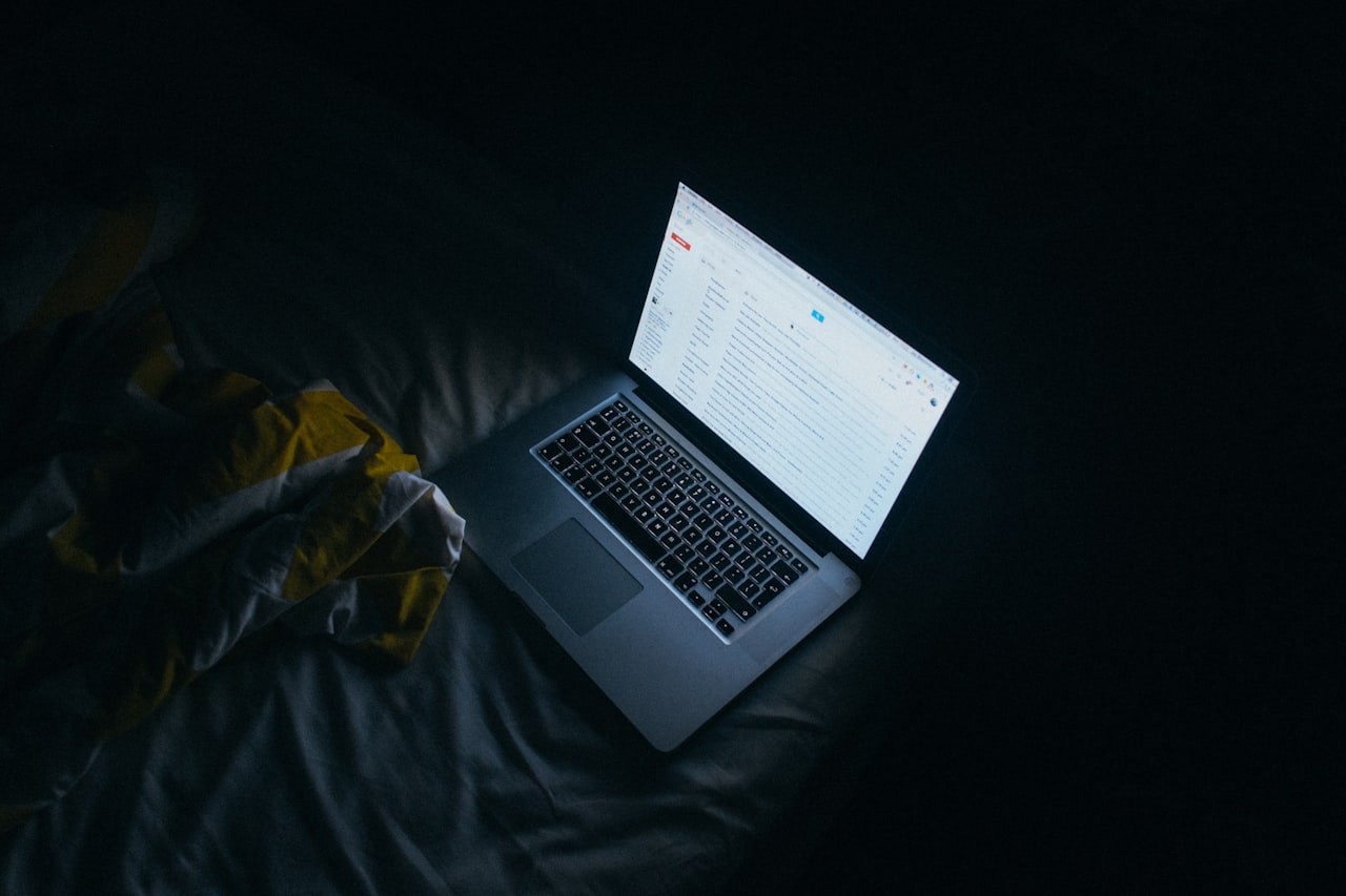 Portátil mostrando una bandeja de correo abierta, iluminando una habitación a oscuras durante la noche